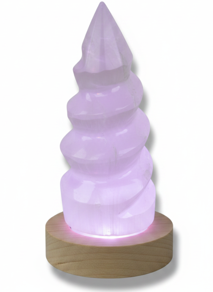 Torre de selenita unicornio sobre base LED de madera irradiando luz violeta